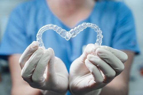 A woman holding Invisalign trays in the shape of a heart