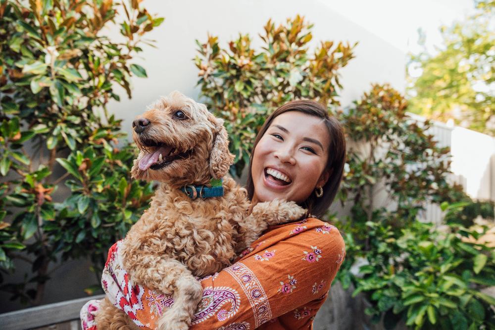 A laughing woman holding her dog outside
