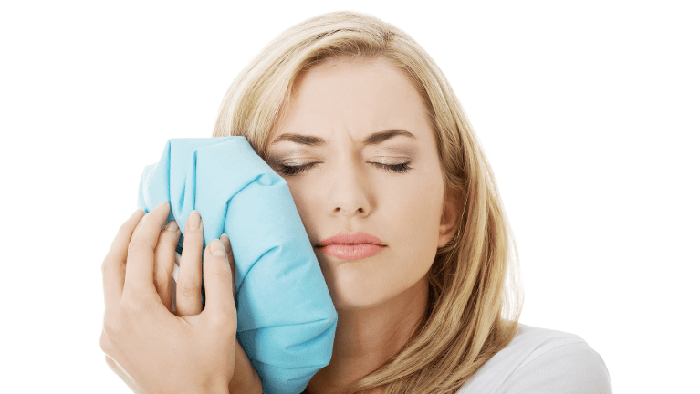 A woman holding an icepack to a painful jaw